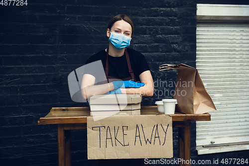 Image of Woman preparing drinks and meals, wearing protective face mask and gloves. Contactless delivery service during quarantine coronavirus pandemic. Take away only concept.