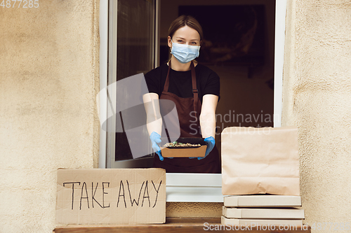 Image of Woman preparing drinks and meals, wearing protective face mask and gloves. Contactless delivery service during quarantine coronavirus pandemic. Take away only concept.