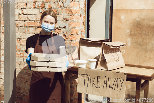 Image of Woman preparing drinks and meals, wearing protective face mask and gloves. Contactless delivery service during quarantine coronavirus pandemic. Take away only concept.