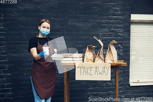 Image of Woman preparing drinks and meals, wearing protective face mask and gloves. Contactless delivery service during quarantine coronavirus pandemic. Take away only concept.