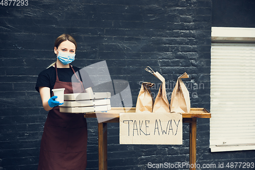 Image of Woman preparing drinks and meals, wearing protective face mask and gloves. Contactless delivery service during quarantine coronavirus pandemic. Take away only concept.