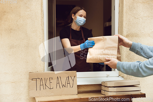 Image of Woman preparing drinks and meals, wearing protective face mask and gloves. Contactless delivery service during quarantine coronavirus pandemic. Take away only concept.