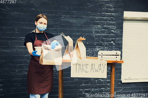 Image of Woman preparing drinks and meals, wearing protective face mask and gloves. Contactless delivery service during quarantine coronavirus pandemic. Take away only concept.