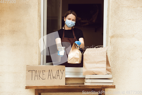 Image of Woman preparing drinks and meals, wearing protective face mask and gloves. Contactless delivery service during quarantine coronavirus pandemic. Take away only concept.