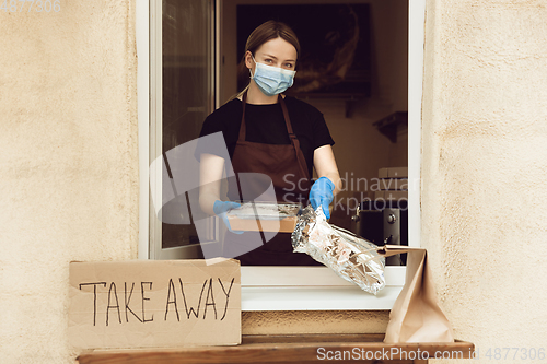 Image of Woman preparing drinks and meals, wearing protective face mask and gloves. Contactless delivery service during quarantine coronavirus pandemic. Take away only concept.