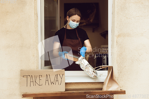 Image of Woman preparing drinks and meals, wearing protective face mask and gloves. Contactless delivery service during quarantine coronavirus pandemic. Take away only concept.