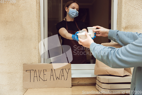 Image of Woman preparing drinks and meals, wearing protective face mask and gloves. Contactless delivery service during quarantine coronavirus pandemic. Take away only concept.