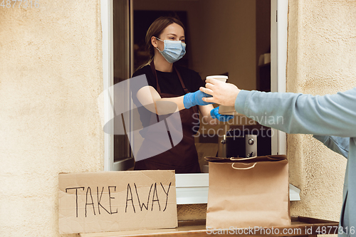 Image of Woman preparing drinks and meals, wearing protective face mask and gloves. Contactless delivery service during quarantine coronavirus pandemic. Take away only concept.