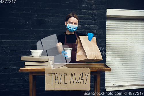 Image of Woman preparing drinks and meals, wearing protective face mask and gloves. Contactless delivery service during quarantine coronavirus pandemic. Take away only concept.