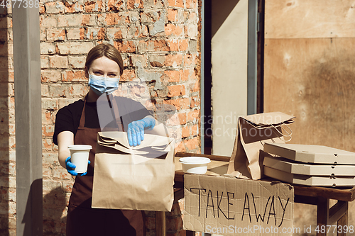 Image of Woman preparing drinks and meals, wearing protective face mask and gloves. Contactless delivery service during quarantine coronavirus pandemic. Take away only concept.