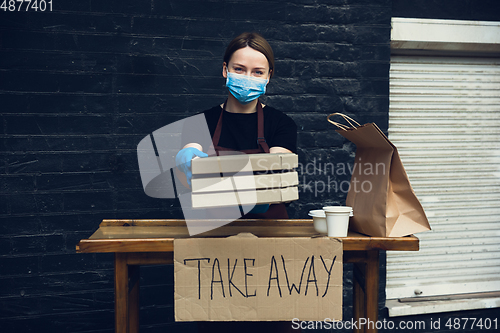 Image of Woman preparing drinks and meals, wearing protective face mask and gloves. Contactless delivery service during quarantine coronavirus pandemic. Take away only concept.