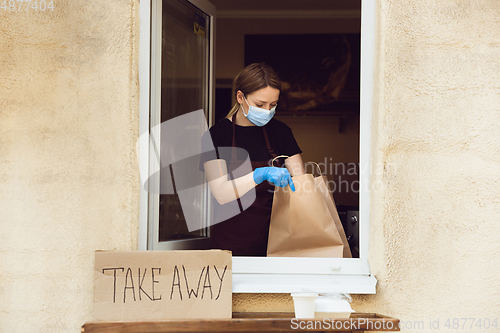 Image of Woman preparing drinks and meals, wearing protective face mask and gloves. Contactless delivery service during quarantine coronavirus pandemic. Take away only concept.