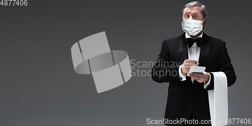 Image of Elegance senior man waiter in protective face mask on gray background. Flyer with copyspace.