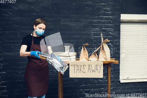 Image of Woman preparing drinks and meals, wearing protective face mask and gloves. Contactless delivery service during quarantine coronavirus pandemic. Take away only concept.