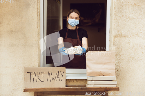 Image of Woman preparing drinks and meals, wearing protective face mask and gloves. Contactless delivery service during quarantine coronavirus pandemic. Take away only concept.