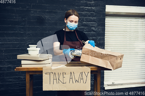 Image of Woman preparing drinks and meals, wearing protective face mask and gloves. Contactless delivery service during quarantine coronavirus pandemic. Take away only concept.