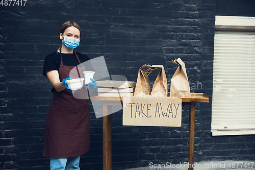 Image of Woman preparing drinks and meals, wearing protective face mask and gloves. Contactless delivery service during quarantine coronavirus pandemic. Take away only concept.