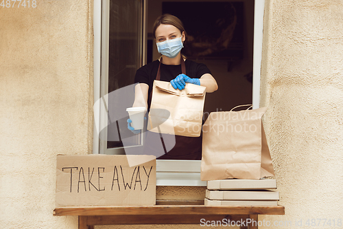 Image of Woman preparing drinks and meals, wearing protective face mask and gloves. Contactless delivery service during quarantine coronavirus pandemic. Take away only concept.