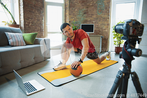 Image of Young caucasian man training at home during quarantine of coronavirus outbreak, doing exercises of fitness, aerobic. Staying sportive during insulation.