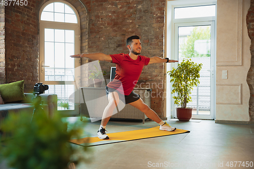 Image of Young caucasian man training at home during quarantine of coronavirus outbreak, doing exercises of fitness, aerobic. Staying sportive during insulation.