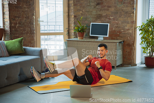 Image of Young caucasian man training at home during quarantine of coronavirus outbreak, doing exercises of fitness, aerobic. Staying sportive during insulation.