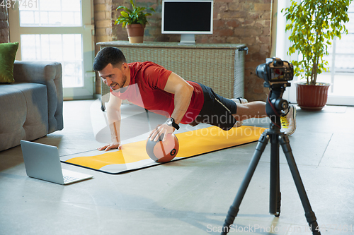 Image of Young caucasian man training at home during quarantine of coronavirus outbreak, doing exercises of fitness, aerobic. Staying sportive during insulation.