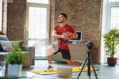 Image of Young caucasian man training at home during quarantine of coronavirus outbreak, doing exercises of fitness, aerobic. Staying sportive during insulation.