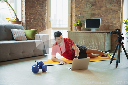 Image of Young caucasian man training at home during quarantine of coronavirus outbreak, doing exercises of fitness, aerobic. Staying sportive during insulation.