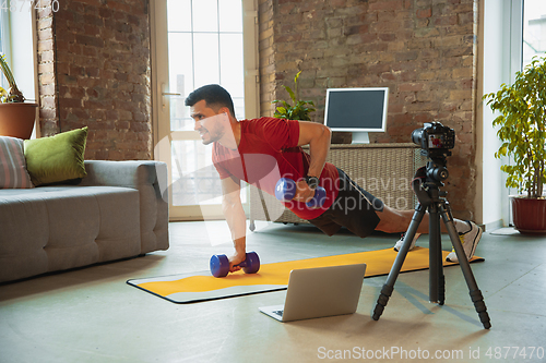 Image of Young caucasian man training at home during quarantine of coronavirus outbreak, doing exercises of fitness, aerobic. Staying sportive during insulation.