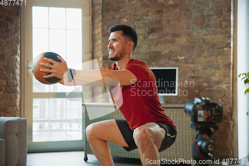 Image of Young caucasian man training at home during quarantine of coronavirus outbreak, doing exercises of fitness, aerobic. Staying sportive during insulation.