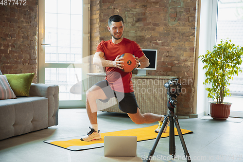 Image of Young caucasian man training at home during quarantine of coronavirus outbreak, doing exercises of fitness, aerobic. Staying sportive during insulation.