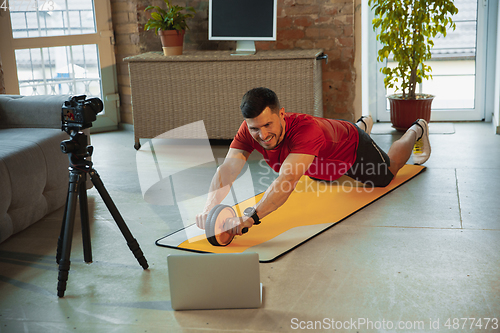 Image of Young caucasian man training at home during quarantine of coronavirus outbreak, doing exercises of fitness, aerobic. Staying sportive during insulation.