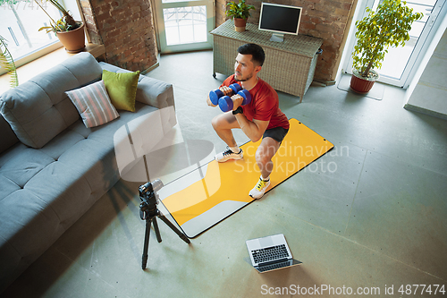 Image of Young caucasian man training at home during quarantine of coronavirus outbreak, doing exercises of fitness, aerobic. Staying sportive during insulation.