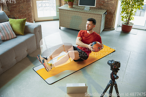 Image of Young caucasian man training at home during quarantine of coronavirus outbreak, doing exercises of fitness, aerobic. Staying sportive during insulation.