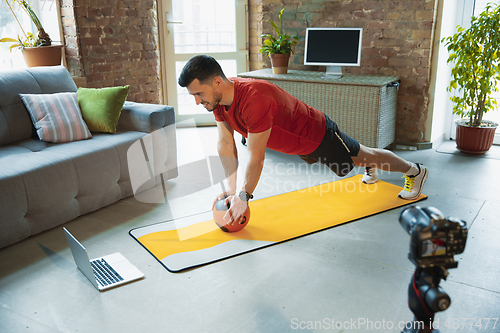 Image of Young caucasian man training at home during quarantine of coronavirus outbreak, doing exercises of fitness, aerobic. Staying sportive during insulation.