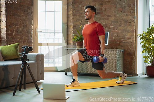 Image of Young caucasian man training at home during quarantine of coronavirus outbreak, doing exercises of fitness, aerobic. Staying sportive during insulation.