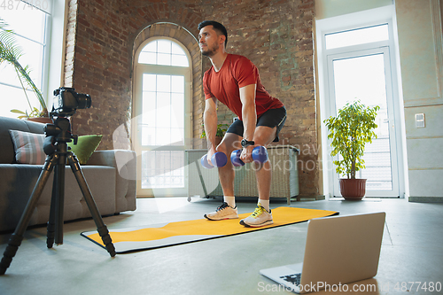 Image of Young caucasian man training at home during quarantine of coronavirus outbreak, doing exercises of fitness, aerobic. Staying sportive during insulation.