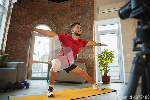 Image of Young caucasian man training at home during quarantine of coronavirus outbreak, doing exercises of fitness, aerobic. Staying sportive during insulation.