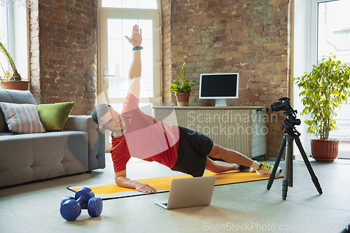 Image of Young caucasian man training at home during quarantine of coronavirus outbreak, doing exercises of fitness, aerobic. Staying sportive during insulation.