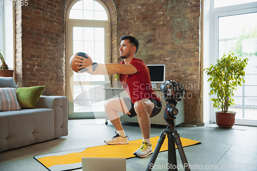 Image of Young caucasian man training at home during quarantine of coronavirus outbreak, doing exercises of fitness, aerobic. Staying sportive during insulation.