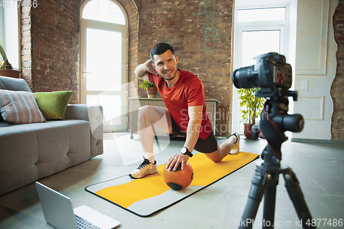 Image of Young caucasian man training at home during quarantine of coronavirus outbreak, doing exercises of fitness, aerobic. Staying sportive during insulation.