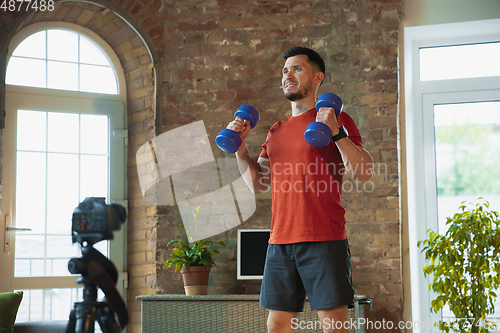 Image of Young caucasian man training at home during quarantine of coronavirus outbreak, doing exercises of fitness, aerobic. Staying sportive during insulation.