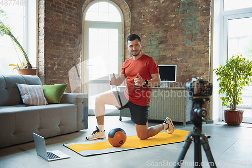 Image of Young caucasian man training at home during quarantine of coronavirus outbreak, doing exercises of fitness, aerobic. Staying sportive during insulation.