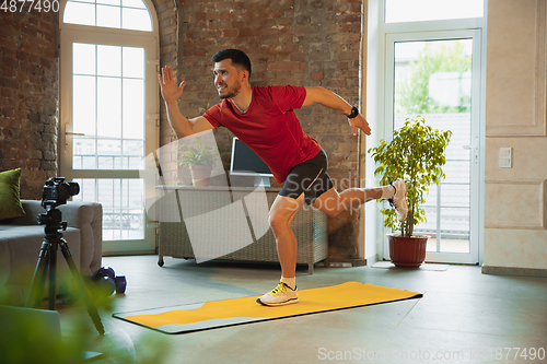 Image of Young caucasian man training at home during quarantine of coronavirus outbreak, doing exercises of fitness, aerobic. Staying sportive during insulation.