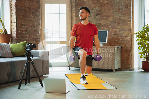 Image of Young caucasian man training at home during quarantine of coronavirus outbreak, doing exercises of fitness, aerobic. Staying sportive during insulation.