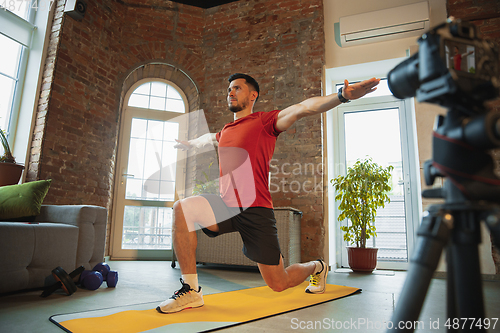 Image of Young caucasian man training at home during quarantine of coronavirus outbreak, doing exercises of fitness, aerobic. Staying sportive during insulation.