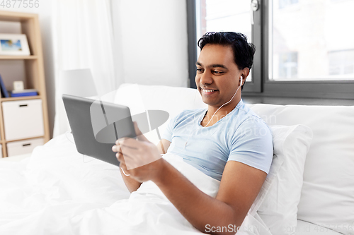 Image of happy indian man with tablet pc in bed at home