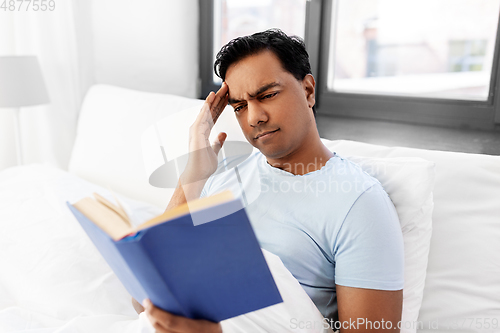 Image of indian man reading book in bed at home
