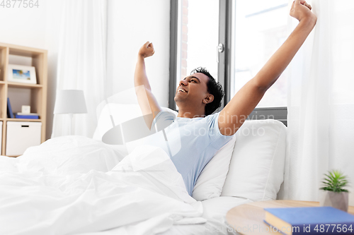 Image of happy smiling indian man lying in bed at home