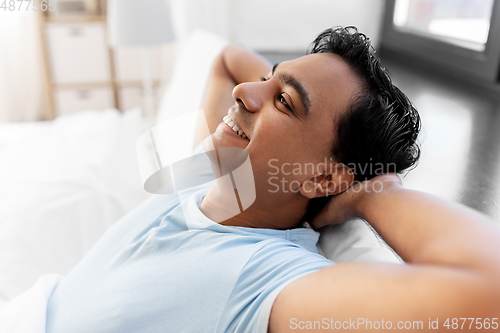 Image of happy smiling indian man stretching in bed at home